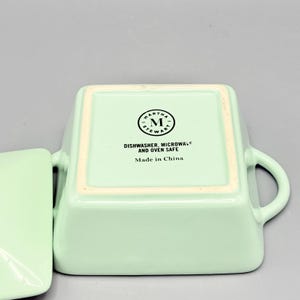 Puede incluir: Un plato cuadrado de cer&aacute;mica verde claro con asas y una tapa a juego. La parte inferior del plato presenta el logotipo de Martha Stewart y el texto "Dishwasher, Microwave and Oven Safe" y "Made in China."