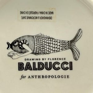 May include: A white ceramic dish with a black and white illustration of a fish. The fish design is by Florence Balducci for Anthropologie. Dishwasher and microwave safe. Made in China.