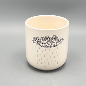 May include: White ceramic mug with a black and white illustration of a cloud with raindrops in pink, blue, and yellow.