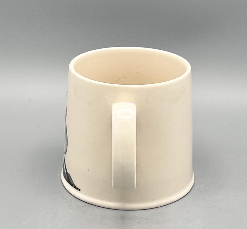 May include: Cream-colored ceramic mug with a white handle. The mug has a cylindrical shape and a simple design, suitable for coffee or tea. The mug is clean and appears unused.