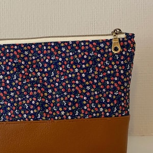 May include: A blue and brown zippered pouch with a floral print. The pouch has a brown leather bottom and a zipper closure with a gold pull.