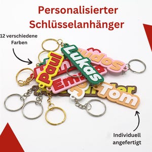 Könnte beinhalten: Eine Sammlung von bunten personalisierten Schlüsselanhängern mit Namen wie "Paul", "Lukas", "Emma", "Tom" und "Jos", mit einer Vielzahl von Farben und einer fetten, verspielten Schriftart. Die Schlüsselanhänger sind aus strapazierfähigem Kunststoff gefertigt und werden mit einem Metallring zum Anbringen an Schlüsseln geliefert.