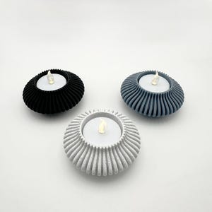 Può includere: Tre portacandele per tealight in diversi colori: nero, grigio e bianco. Ogni portacandele ha un design testurizzato e scanalato con una piccola apertura rotonda per una candela tealight.