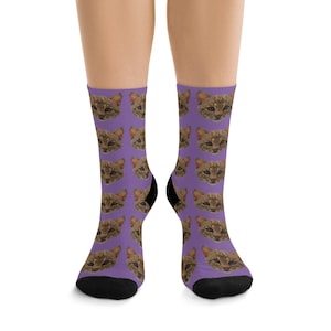 Peut inclure: Une paire de chaussettes violettes avec un motif répété de visage de chat. Les chaussettes sont noires au niveau des orteils et des talons.
