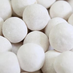 Può includere: Primo piano di un mucchio di caramelle bianche e rotonde. Le caramelle hanno una superficie leggermente ruvida e sono raggruppate, riempiendo l'inquadratura. L'illuminazione è morbida, evidenziando le forme e le trame delle caramelle.