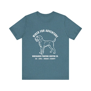 May include: Teal t-shirt featuring a white Wirehaired Pointing Griffon dog graphic and the text "WIRED FOR ADVENTURE." Beneath the dog is the text "WIREHAIRED POINTING GRIFFON CO." and the words "EST. LOYAL | RUGGED | SCRUFFY."