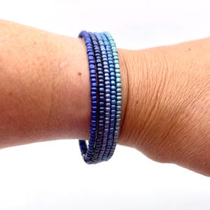 May include: A multi-strand bracelet composed of small, uniform seed beads arranged in a color gradient. The beads transition from a deep, dark navy blue on one side to a lighter, bright sky blue on the other, creating a smooth ombre effect.