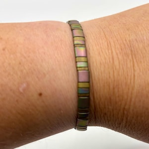 May include: A close-up of a bracelet with rectangular, iridescent beads. The beads shift in colour, displaying hues of pink, green, and gold. The bracelet is worn on a wrist, showcasing its design and colour variations.