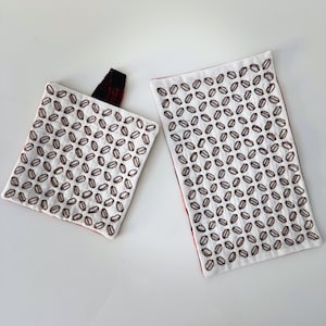 May include: A square quilted potholder with a black hanging loop and a rectangular quilted mat, both featuring a white fabric surface with a repeating pattern of small, brown, diamond-shaped embroidered outlines and a red fabric backing.