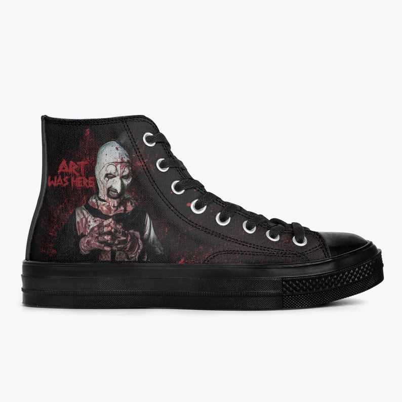 May include: Black high-top trainer with a horror-themed graphic. The design features a character with a white mask and the text "ART WAS HERE" in red. The trainer has a black sole and white laces.