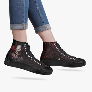 May include: Black high-top trainers with white laces and a thick black sole. One trainer features a graphic of a character with the text "ART WAS HERE". The other trainer has a red speckled design.