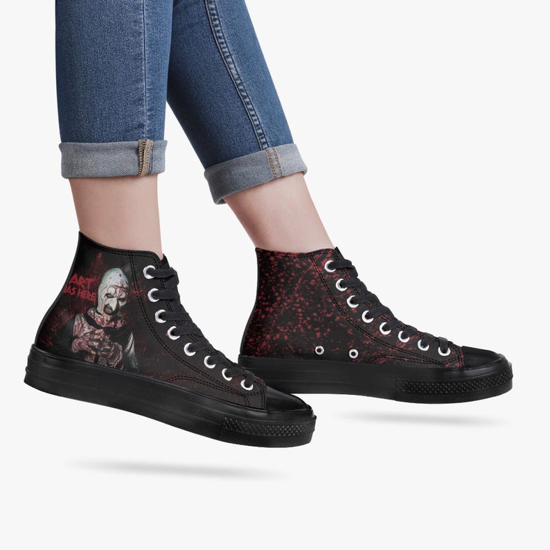 May include: Black high-top trainers with white laces and a thick black sole. One trainer features a graphic of a character with the text "ART WAS HERE". The other trainer has a red speckled design.