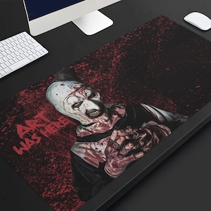 May include: A black desk mat with a scary clown design, featuring white face paint, red details, and the text "ART WAS HERE." The background has a dark red splatter effect. A computer, keyboard, and mouse are visible.