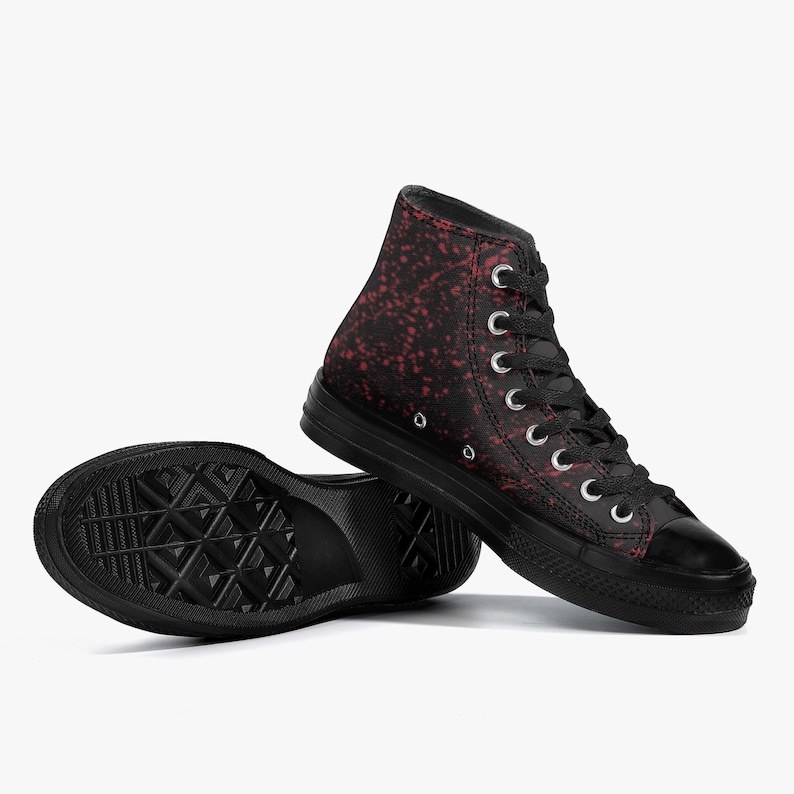 May include: Black high-top trainers with a red speckled pattern. The trainers have black laces, a black rubber sole, and a black toe cap. The shoes are set against a white background.