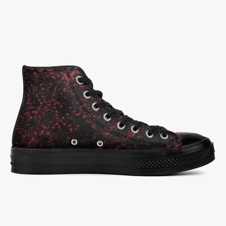 May include: Black high-top trainers with a red speckled pattern. The trainers have a black rubber sole and toe cap, with silver eyelets for the laces. The design is a bold statement, suitable for casual wear.