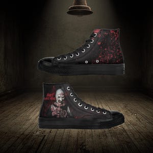 May include: Black high-top trainers with a horror-themed design. One trainer features a splatter pattern in red, while the other displays a character with the text "ART WAS HERE". The trainers have black soles and white laces.