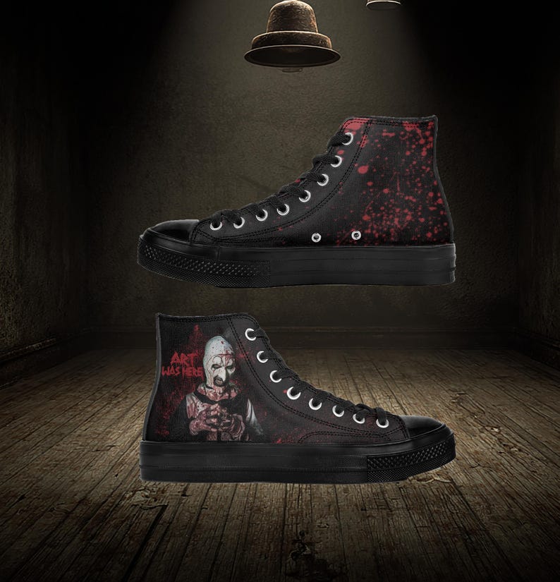 May include: Black high-top trainers with a horror-themed design. One trainer features a splatter pattern in red, while the other displays a character with the text "ART WAS HERE". The trainers have black soles and white laces.