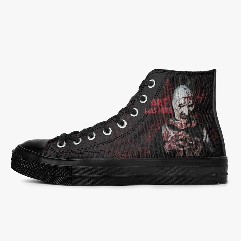 May include: Black high-top canvas trainers with a horror-themed graphic. The design features a character with a white mask and the text "ART WAS HERE" in white. The background is a dark red splatter effect.