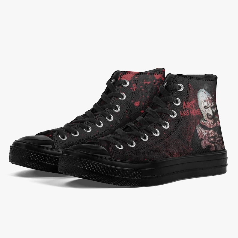 May include: Pair of black high-top trainers with a horror-themed design. The trainers feature a black rubber sole, black laces, and a graphic of a scary clown with the text "ART WAS HERE" on the side. Red splatter details add to the spooky aesthetic.