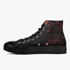 May include: Black high-top canvas trainer with a platform sole. The shoe features a black base with a red splatter design. It has white eyelets and laces. The toe cap and sole are solid black.