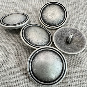 May include: Four silver-toned buttons with a raised, rounded surface and a textured, aged finish. The buttons have a double-rimmed border.