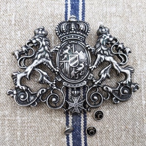 May include: A silver metal coat of arms with two lions, a crown, and a shield with the word "BAYERN" on it.