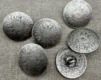 May include: Six silver-toned metal buttons with a raised design of an eagle and the text "1 Corona 1819" on the front. The buttons have a smooth, slightly textured surface.