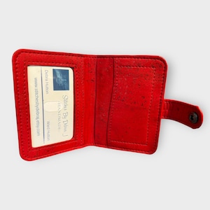 May include: Open red wallet with a snap closure. The wallet is made of a textured material and has a clear window for a card. The interior has slots for cards and cash. The text "Stitches By Debra J Handmade" is visible.