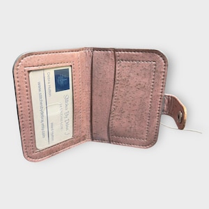 May include: Open, light pink wallet with a snap closure. The wallet is made of a textured material and has a card slot. The text "Stitches By Diva J Handmade" is visible on a card inside the wallet.
