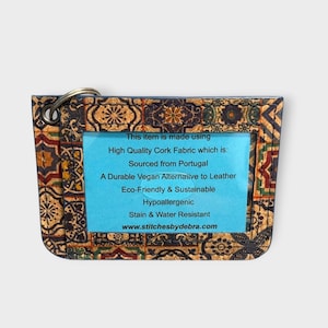 May include: A rectangular cork fabric item with a metal ring, featuring a colorful mosaic pattern. A blue rectangle in the center contains text about the item's features, including being sourced from Portugal and a vegan alternative to leather.