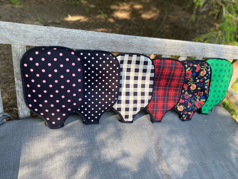 Pu&ograve; includere: Sei diverse racchette da pickleball con motivi diversi, tra cui pois rosa e neri, pois neri e bianchi, gingham bianco e nero, tartan rosso e nero, floreali e verdi.
