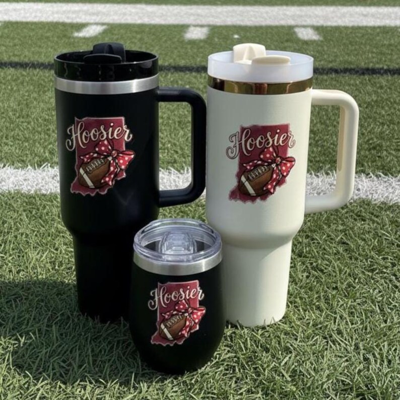 May include: Three insulated tumblers in black and cream colors, and a black wine tumbler. Each tumbler features the word "Hoosier" with a football and bow graphic. The tumblers have handles and lids, perfect for hot or cold beverages.