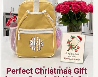 May include: A mustard yellow backpack with white trim and a floral monogram featuring the letters AKH. Beside it sits a greeting card with a pickleball paddle illustration, a Santa hat, and the text: To my Best Coach and Mom. Merry Christmas!