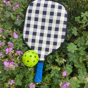 Pu&ograve; includere: Una racchetta da paddleball a scacchi bianco e nero con un manico blu e una pallina da paddleball verde.