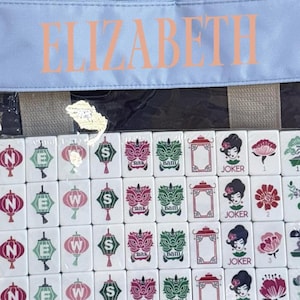 May include: A set of white Mahjong tiles with red, green, and black symbols and characters. The tiles are in a clear bag with the name "ELIZABETH" printed in peach. The bag is light blue.