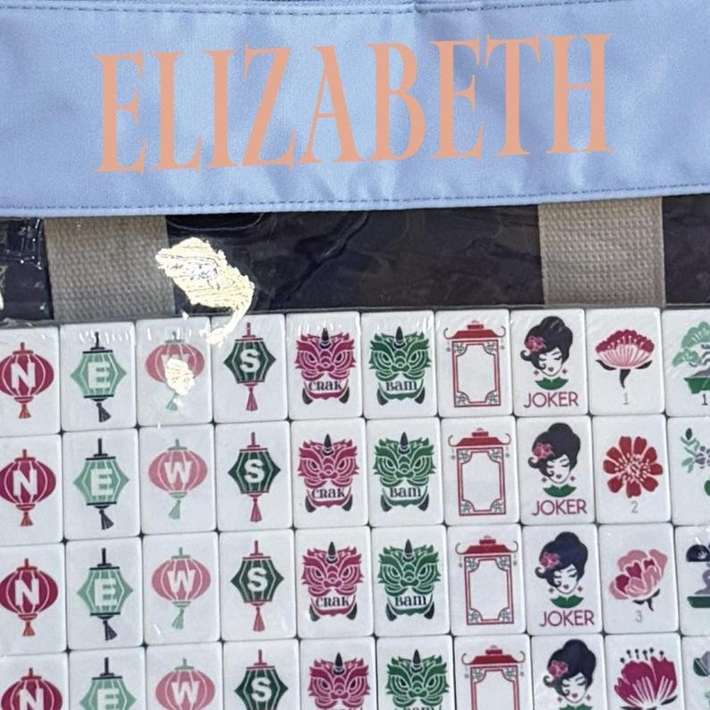 May include: A set of white Mahjong tiles with red, green, and black symbols and characters. The tiles are in a clear bag with the name "ELIZABETH" printed in peach. The bag is light blue.