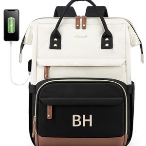 May include: A black and white canvas backpack with brown leather accents. The backpack has a large main compartment and a smaller front pocket. The front pocket has a zipper closure and the initials "BH" embroidered on it. The backpack has a USB charging port on the side.