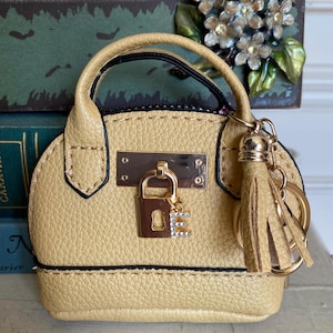 May include: A small, yellow faux leather handbag with a gold lock and key charm. The handbag has a top handle and a tassel keychain.