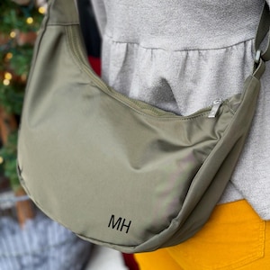 May include: A green, crescent-shaped shoulder bag with a zipper closure and the initials "MH" embroidered on the front.