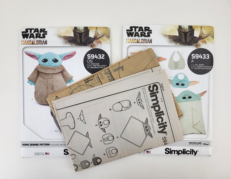 K&ouml;nnte beinhalten: Zwei Star Wars Mandalorian N&auml;hvorlagen. Ein Schnittmuster zeigt eine Grogu-Pl&uuml;schpuppe, das andere eine Grogu-L&auml;tzchen und eine Decke. Die Muster sind von Simplicity und enthalten den Text "S9432 OS" und "S9433 A".