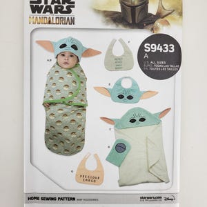 K&ouml;nnte beinhalten: Ein Simplicity-Schnittmuster f&uuml;r Babyzubeh&ouml;r mit Designs, die von The Mandalorian inspiriert sind. Das Muster enth&auml;lt Anleitungen f&uuml;r einen Grogu-Hut, eine Wickeldecke, eine L&auml;tzchen und ein Kapuzenhandtuch. Die Verpackung zeigt das Star Wars-Logo und den Text "PRECIOUS CARGO".