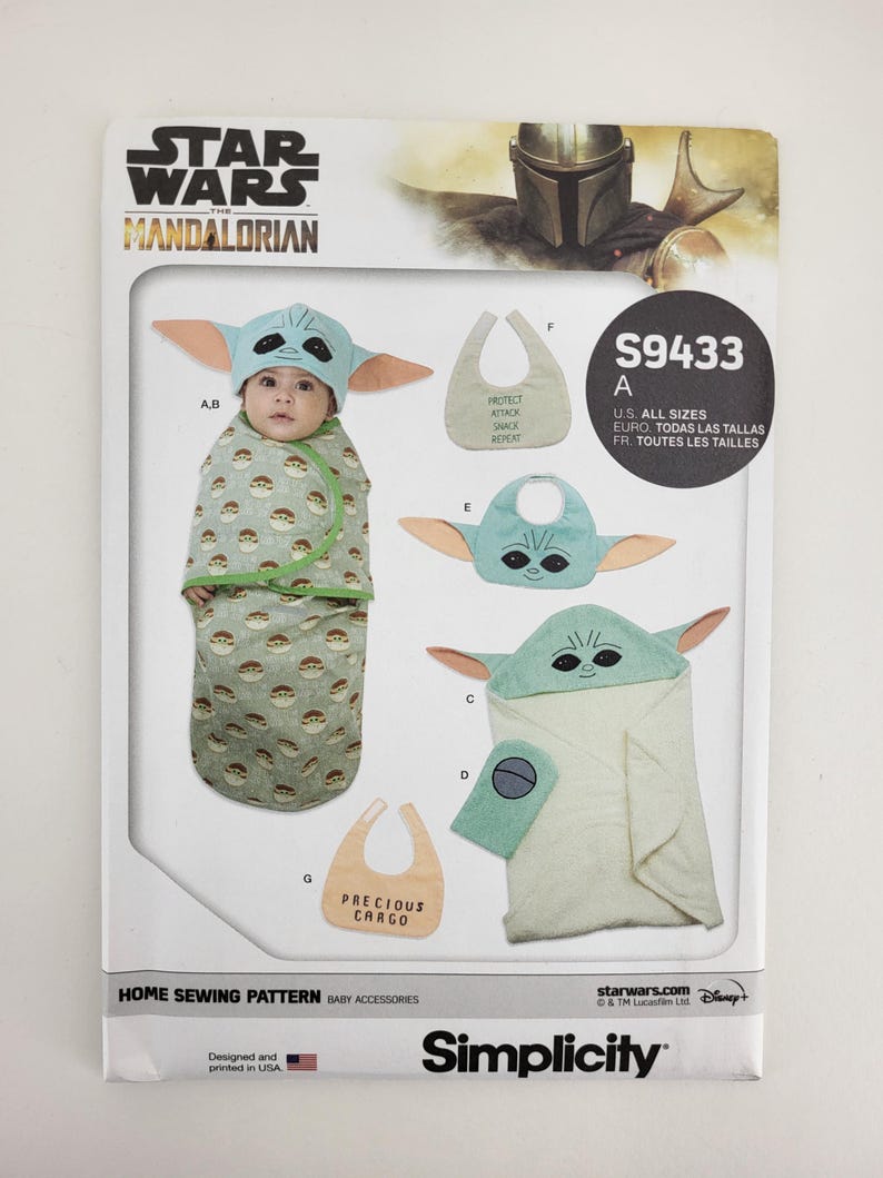 K&ouml;nnte beinhalten: Ein Simplicity-Schnittmuster f&uuml;r Babyzubeh&ouml;r mit Designs, die von The Mandalorian inspiriert sind. Das Muster enth&auml;lt Anleitungen f&uuml;r einen Grogu-Hut, eine Wickeldecke, eine L&auml;tzchen und ein Kapuzenhandtuch. Die Verpackung zeigt das Star Wars-Logo und den Text "PRECIOUS CARGO".