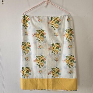 Peut inclure: Un drap de lit blanc à fleurs avec des roses jaunes et une bordure jaune. Le drap est suspendu à un cintre rose.