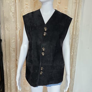 Può includere: Un gilet in camoscio nero con scollo a V e bottoni color oro. Il gilet è senza maniche e ha un design classico. I bottoni sono decorativi e aggiungono un tocco di eleganza all'indumento. Questo gilet è un'aggiunta elegante a qualsiasi guardaroba.