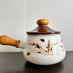 May include: White enamel saucepan with a brown lid and a wooden handle. The saucepan has a floral design of brown wheat stalks and leaves.
