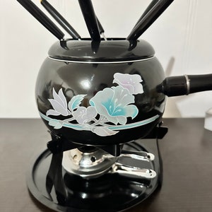 May include: Black fondue pot with a floral design and six fondue forks. The pot is on a black stand with a silver burner.