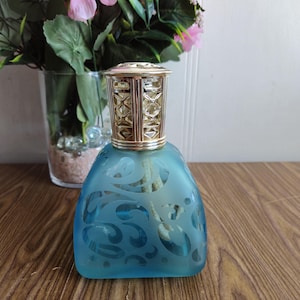 Peut inclure: Un diffuseur d'huiles essentielles en verre bleu avec un dessus en métal doré et un motif gravé décoratif. Le diffuseur a une mèche blanche.