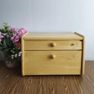 Op de afbeelding: Een houten broodtrommel met twee laden. De laden hebben ronde houten knoppen. De broodtrommel is lichtbruin en heeft een natuurlijke houten afwerking.