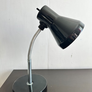 Peut inclure: Une lampe de bureau noire avec un bras flexible en col de cygne et une base ronde. La lampe a un abat-jour en métal noir.