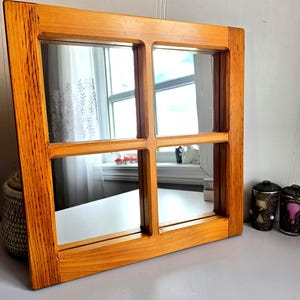 Peut inclure: Un miroir encadré de bois avec un design de carreaux de fenêtre. Le cadre est en bois brun clair et a une forme rectangulaire avec quatre carreaux. Le miroir reflète l'environnement, y compris une fenêtre et des objets décoratifs.